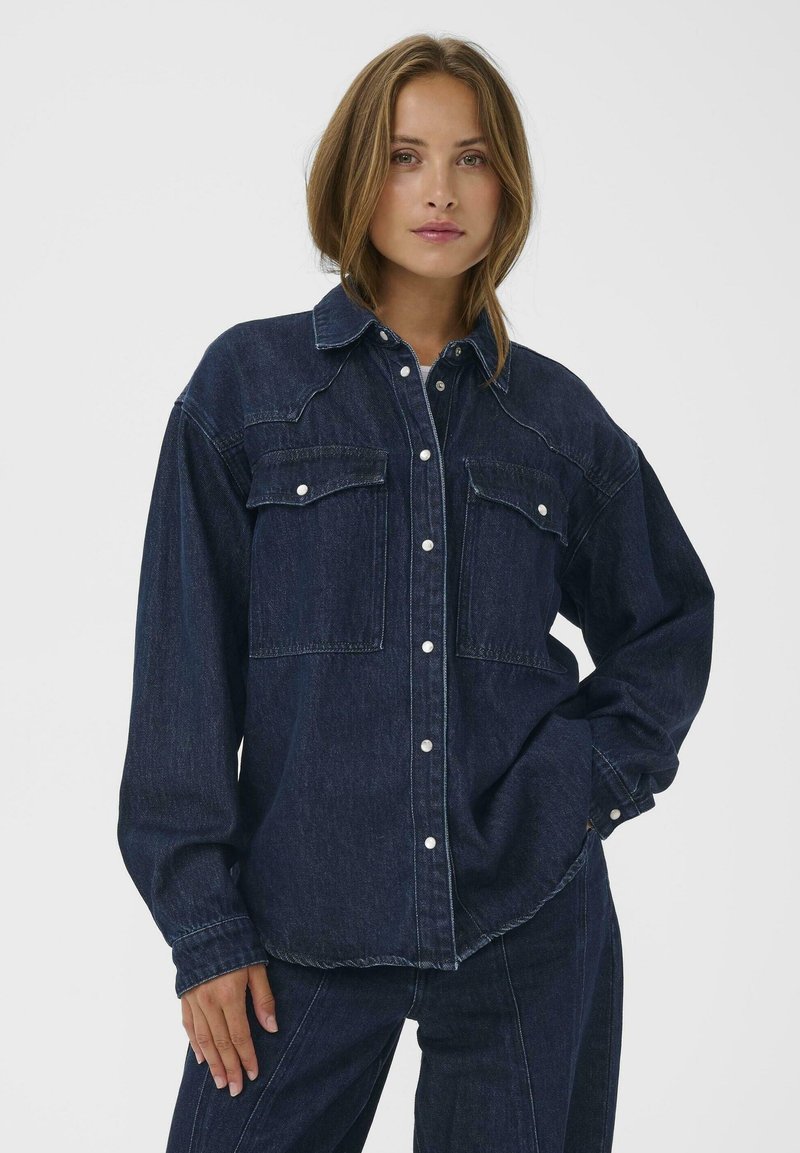 Donkerdenim shirt met een kraag, twee borstzakken en knoopsluiting. Kenmerkt zichtbare stiksels en een ontspannen pasvorm ontwerp.