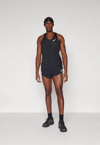 Fekete sportos atlétafelső és rövidnadrág Nike logóval. Az anyag könnyűnek tűnik. A férfi fekete fejpántot és fekete sportcipőt visel.