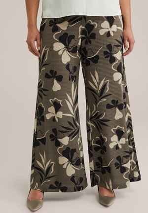 Wijde broek van een textuurstof met een bloemenpatroon in zwart en room tegen een olijfgroene achtergrond.