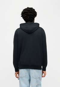 Μαύρο φούτερ με κουκούλα σε χαλαρή γραμμή, με ριμπ τελείωμα και μανσέτες. Ομαλή υφή, απλό σχέδιο και τσέπη καγκουρό στο μπροστινό μέρος.