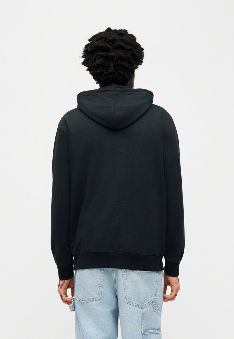 Sweat-shirt à capuche noir à coupe décontractée, ourlet et poignets côtelés. Texture lisse, design uni, avec une poche kangourou visible à l'avant.