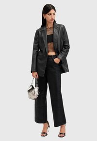 Černý kožený blazer přes průhledný černý krajkový crop top, spárovaný s širokými černými džíny a metalickou kabelkou; černé sandály na vysokém podpatku.