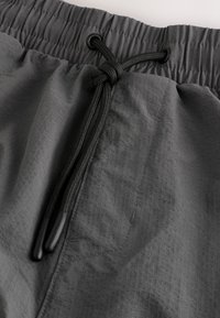 Grijze shorts met een elastische tailleband en een gestructureerde stof, voorzien van een zwart trekkoord in de taille en versterkte stiksels langs de naden.