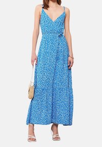Blauwe bloemen maxi-jurk met spaghettibandjes, een wikkelontwerp, een gelaagde rok en een strikdetail in de taille. Glad materiaal met een lichte textuur.