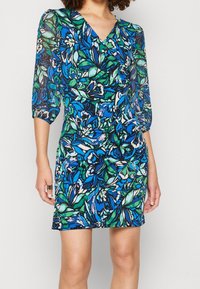 Vestido cruzado de manga corta con estampado floral en azul, verde y blanco. Presenta un escote en V y una forma entallada, confeccionado con tela ligera.