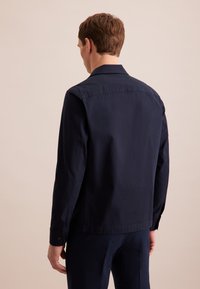 Giacca blu navy realizzata in tessuto leggero, caratterizzata da un colletto a punta, maniche lunghe e polsini bottonati, con un design pulito e minimalista.