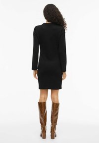 Czarna sukienka na długi rękaw o dopasowanym kroju, wykonana z miękkiego materiału. Para brązowych połyskliwych kozaków do kolan na szerokim obcasie.