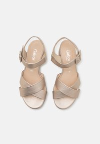 Sandali in pelle tan con design a fasce incrociate e chiusura con fibbia. Texture liscia con una leggera lucentezza. Suola in gomma per aderenza e comfort.