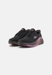 Black athletic shoes with a mesh upper, featuring pink accents and a textured sole. Includes laces and a branded logo on the side.