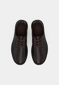 Pair of dark brown leather lace-up shoes with black soles viewed from above on a white background.