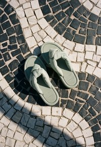 Tongs vert clair rembourrées placées sur un pavement circulaire en mosaïque de pavés noirs et blancs au soleil.