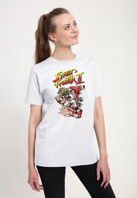 Bílé tričko s barevným grafickým vyobrazením "Street Fighter II", na kterém jsou postavy v akčních pozicích. Klasický kulatý výstřih.