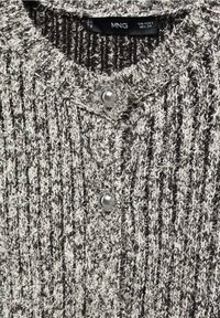 Maglione a coste grigio e bianco con colletto rotondo, due bottoni argentati e una superficie texturizzata.