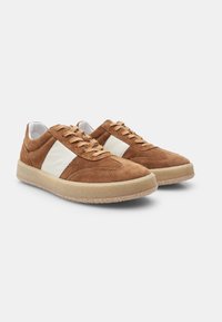 Sneaker in suede marrone con dettagli in pelle bianca, punta rotonda e suola in gomma testurizzata. Presenta lacci piatti e un collare imbottito.