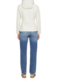 Hoodie blanc matelassé avec une taille ajustée et une capuche, associé à un jean droit bleu clair et des baskets beiges avec des accents à motifs.