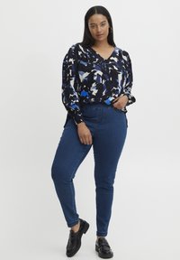 Blusa de manga larga con un patrón abstracto en azul, negro y blanco; combinada con jeans ajustados azules y mocasines negros.