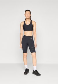 Schwarzes sportliches Crop-Top und Radlerhosen mit glatter Textur, figurbetontem Schnitt und seitlichen Mesh-Einsätzen, kombiniert mit schwarzen Sneakers.