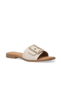 Beige lædersandal med bred rem og et stort guldspænde. Flad sål med en lysebrune base og struktureret overdel.