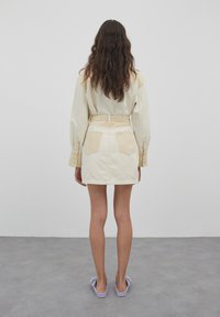 Crème overhemd met lange mouwen, gecombineerd met een beige denim minirok met achterzakken en een riem. Lavendelkleurige schoenen maken de look compleet.