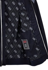 Innenbereich der Marinejacke mit einem diamantge quilteten Muster und Logos. Verfügt über eine Handytasche mit einem roten Etikett, grauen Hardware und kontrastierenden Verzierungen.