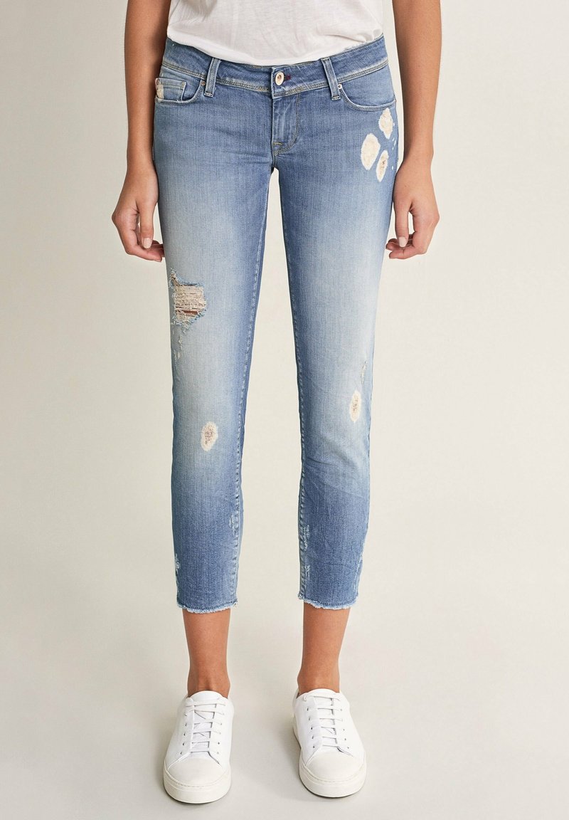 Svetle modré džíny s krátkou délkou, s třenými okraji a opotřebovanými záplatami. Nosené s bílými teniskami.