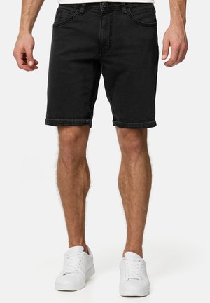 Shorts en denim noir avec une coupe droite, ourlets retroussés, cinq poches et détails de couture subtils, associés à des baskets blanches.