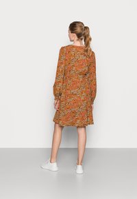 Vestido floral em tom de ferrugem, com mangas longas, decote redondo e bainha babada. Combinado com ténis brancos; apresentado contra um fundo branco liso.