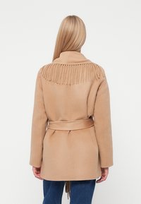 Bež villane coat vöötidega, millel on krae ääres frantsi detail ja pikad varrukad. Lõige on veidi laiem.