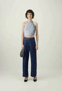 Denim halter crop top, plave široke traperice, crne cipele s visokim potpeticama i mala crna torba, smješteni na neutralnoj pozadini.