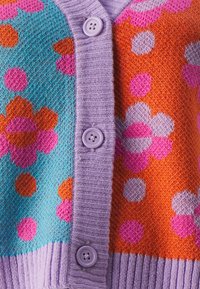 Färgglad stickad kofta med lila, turkos, orange och rosa färger samt blommönster och prickar. Fem lila knappar längs fram.