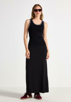 Sort ribbet tanktop med hvid kant, parret med et langt sort nederdel og mørke sneakers. Modellen har solbriller på og viser et afslappet look.
