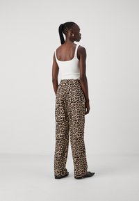 Hvit ribbet tanktop og leopardmønstrede vide bukser, som kombinerer beige, svart og brunt mønster. Glatt tekstur med en avslappet passform.