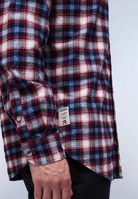 Rood, marineblauw en wit geruit flanellen overhemd met zichtbare stiksels, een label aan de onderzijde en knoopmanchetten. Zachte structuur, relaxte pasvorm.