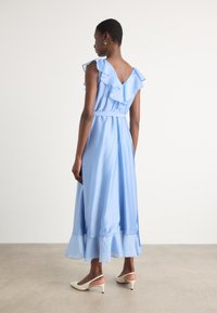 Light blue, knee-length dress with ruffled shoulders, cinched waist, and a flared hem. Worn with white slingback heels. Smooth fabric texture.