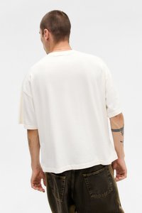 Short-sleeve, crew-neck t-shirt in off-white cotton fabric with a relaxed fit. Features stitched hems and slightly dropped shoulders.