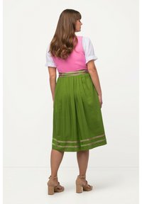 Gonna verde a pieghe con dettagli rosa e corpino rosa aderente, abbinata a una camicia bianca. Sandali beige con tacco alto completano l'outfit.
