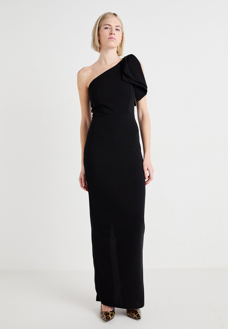 Black one-shoulder dress with a ruffled detail at the shoulder, fitted silhouette, and a side slit, complemented by leopard-print heels.
