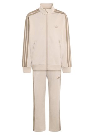Beżowy dres Adidas z kurtką na zamek, kieszeniami bocznymi oraz pasującymi spodniami z trzema brązowymi paskami wzdłuż rękawów i nóg.