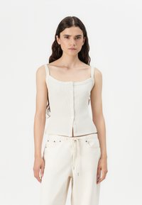 White ribbed tank top with a square neckline and button closure, paired with cream-colored, drawstring waist pants. Soft texture, minimal design.