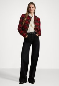 Sarkana un zaļa šķērsota vilnas jaka ar apaļu dekoltē, valkāta uz baltas blūzes. Apvienota ar augsto jostasvietu melnām platām biksēm.