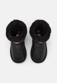 Bottes noires imperméables jusqu'à la cheville avec une doublure intérieure en peluche, un bout rond et un patch décoratif. Extérieur texturé avec un col doux et pelucheux.