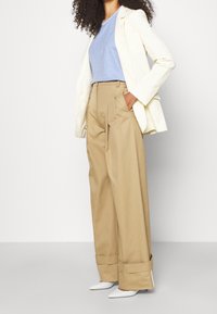 Blazer crema sobre una blusa azul clara, combinado con pantalones de pierna ancha de cintura alta en color beige. Zapatos blancos de punta, con textura suave y corte ajustado.