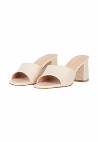 Mule beige con punta aperta realizzate in materiale sintetico liscio, dotate di una larga fascia frontale e di un tacco a blocco spesso. Suola piatta per il massimo comfort.