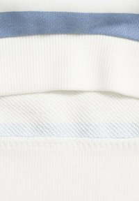 Strati di tessuto a maglia in bianco con una striscia orizzontale blu. Presenta motivi testurizzati e lisci, con finiture a coste e intrecciate.