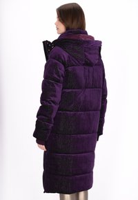 Długa puchowa kurtka w głębokim fioletowym kolorze o połyskującej fakturze, z kapturem, pikowanym wzorem i dopasowanymi mankietami. Widoczne regulowane elementy metalowe.