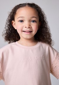 Svetloružová bavlnená mikina s vyšívaným nápisom "ALLSAINTS" a čipkovým detailom na krátkych rukávoch. Mäkká textúra, voľný strih.