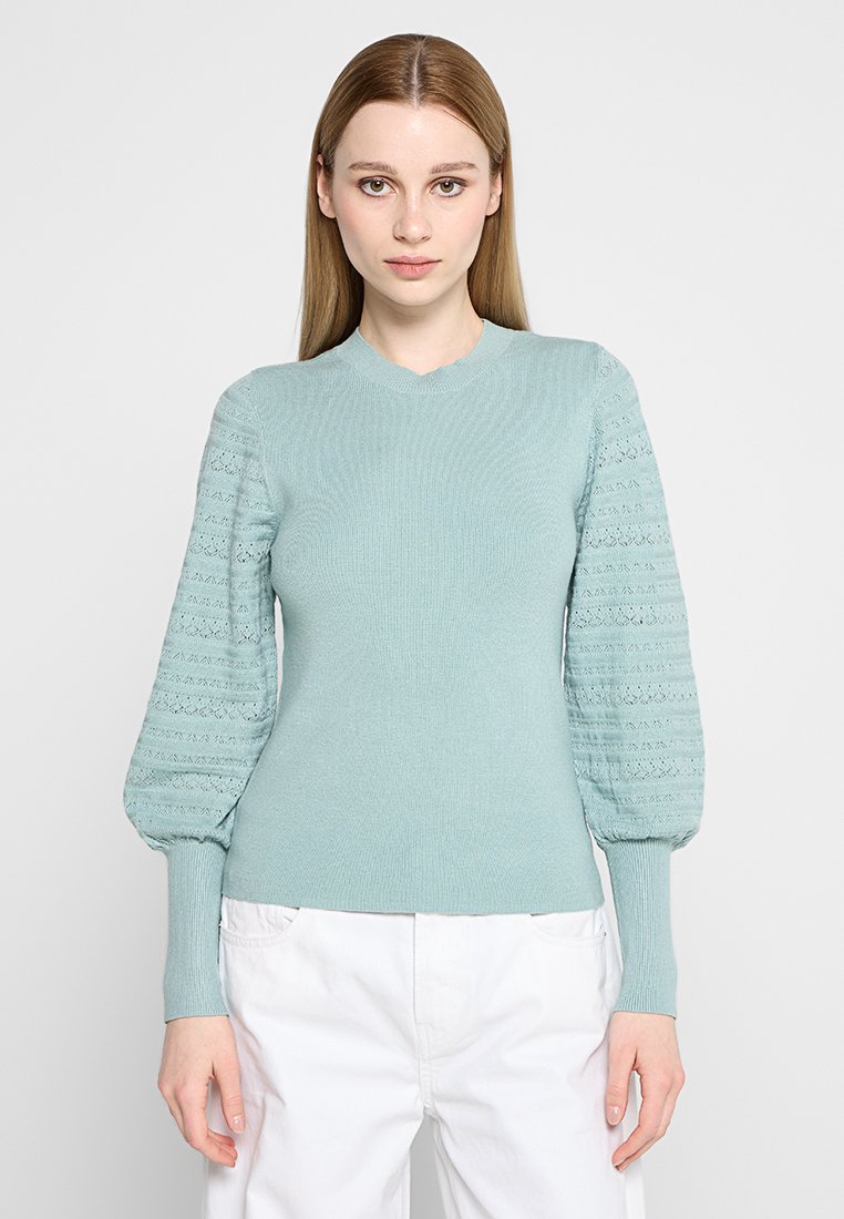 Lichtblauwe gebreide trui met opgezette mouwen, voorzien van een gestructureerd patroon. Getailleerde torso met ribbelzoom en ronde halslijn.