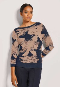 Marineblauer und beiger gestrickter Pullover mit floralem Muster, weitem Bootsausschnitt, Dreiviertelärmeln und gerippten Bündchen, kombiniert mit dunklen Hosen.