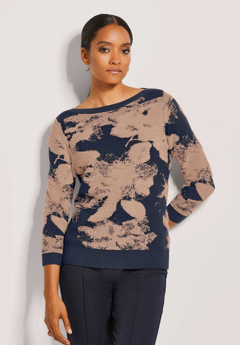 Marineblauer und beiger gestrickter Pullover mit floralem Muster, weitem Bootsausschnitt, Dreiviertelärmeln und gerippten Bündchen, kombiniert mit dunklen Hosen.