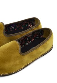 Miękkie zamszowe musztardowo-żółte buty wsuwane z brązowym wykończeniem i kolorowym wnętrzem w paisley, z detalicznym haftem na krawędziach podeszwy.